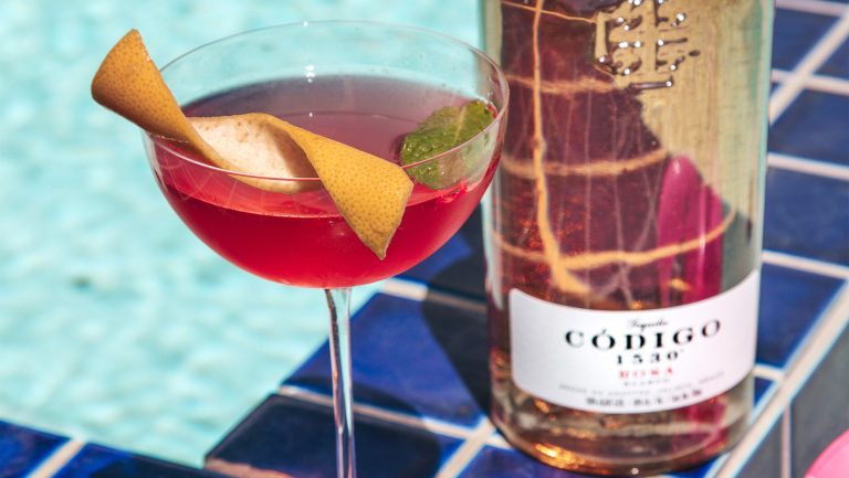 Pink tequila cocktail serves in a coupe glass garnished with a twist of lemon