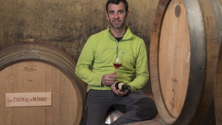 Florian André rests with a glass of wine on some Château de Manissy barrels