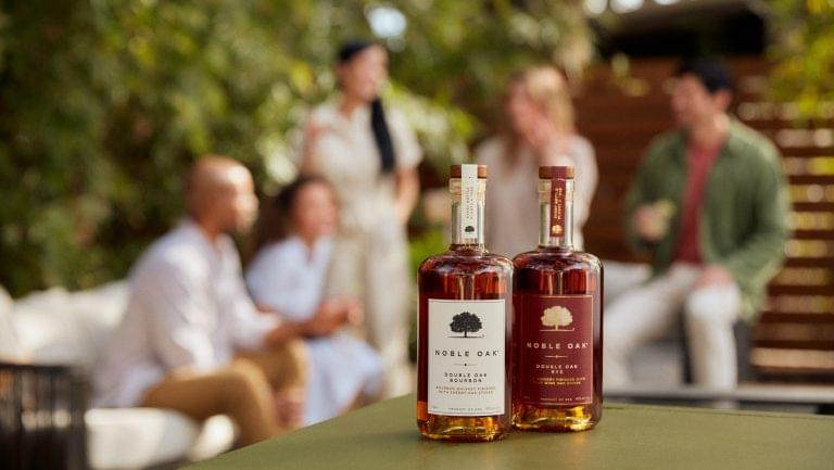 Two bottles of Noble Oak in the foreground, with a party of people in the background