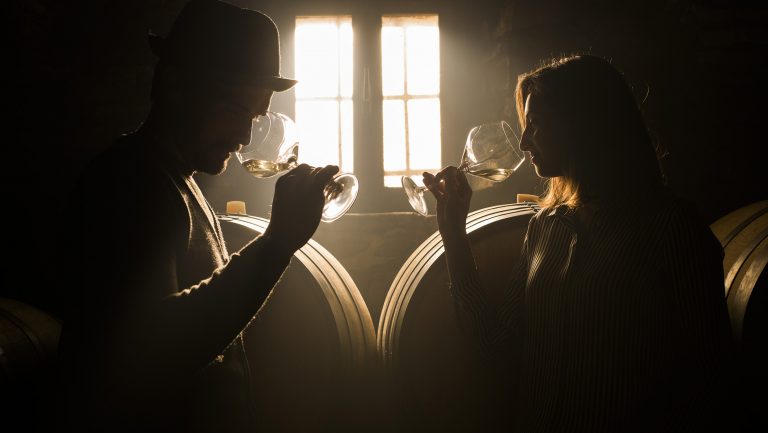 Two silhouetted people sample glasses of wine