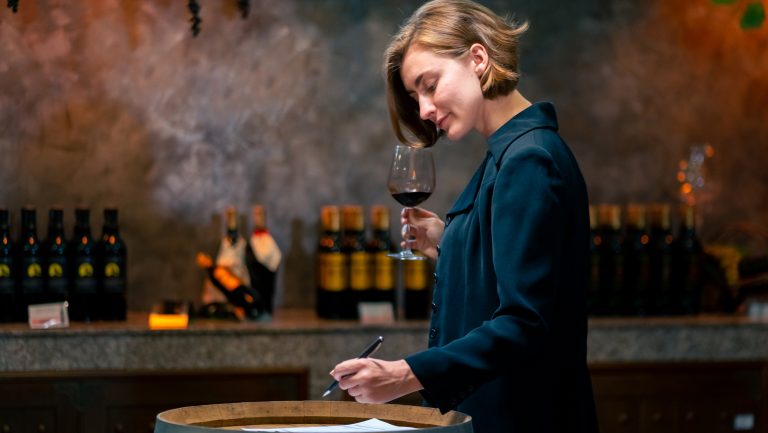 A female sommelier holds a glass of red wine while checking something on her tablet