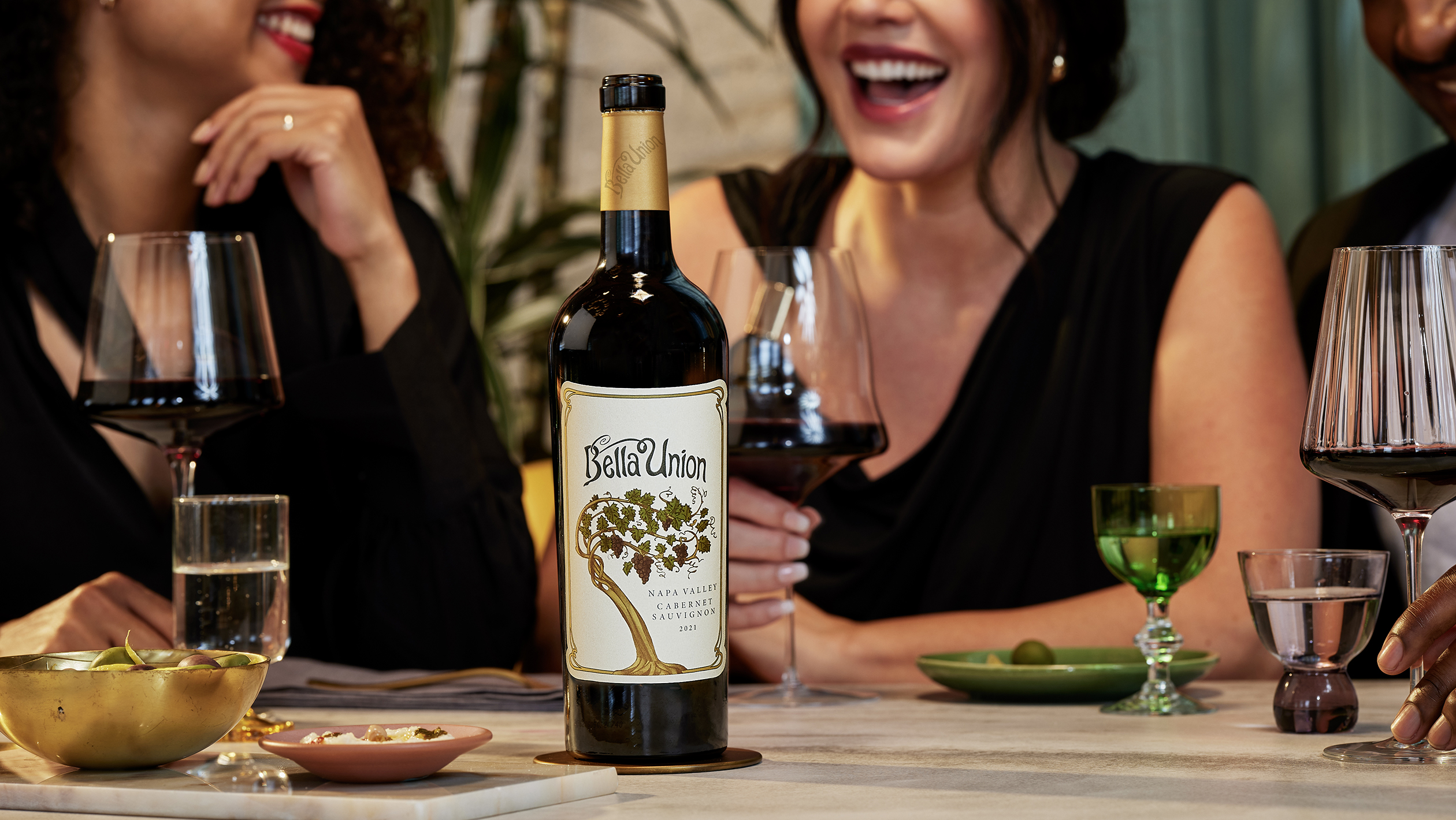 A bottle of Bella Union Cabarnet Sauvignon sits in the foreground of a table of excited wine drinkers
