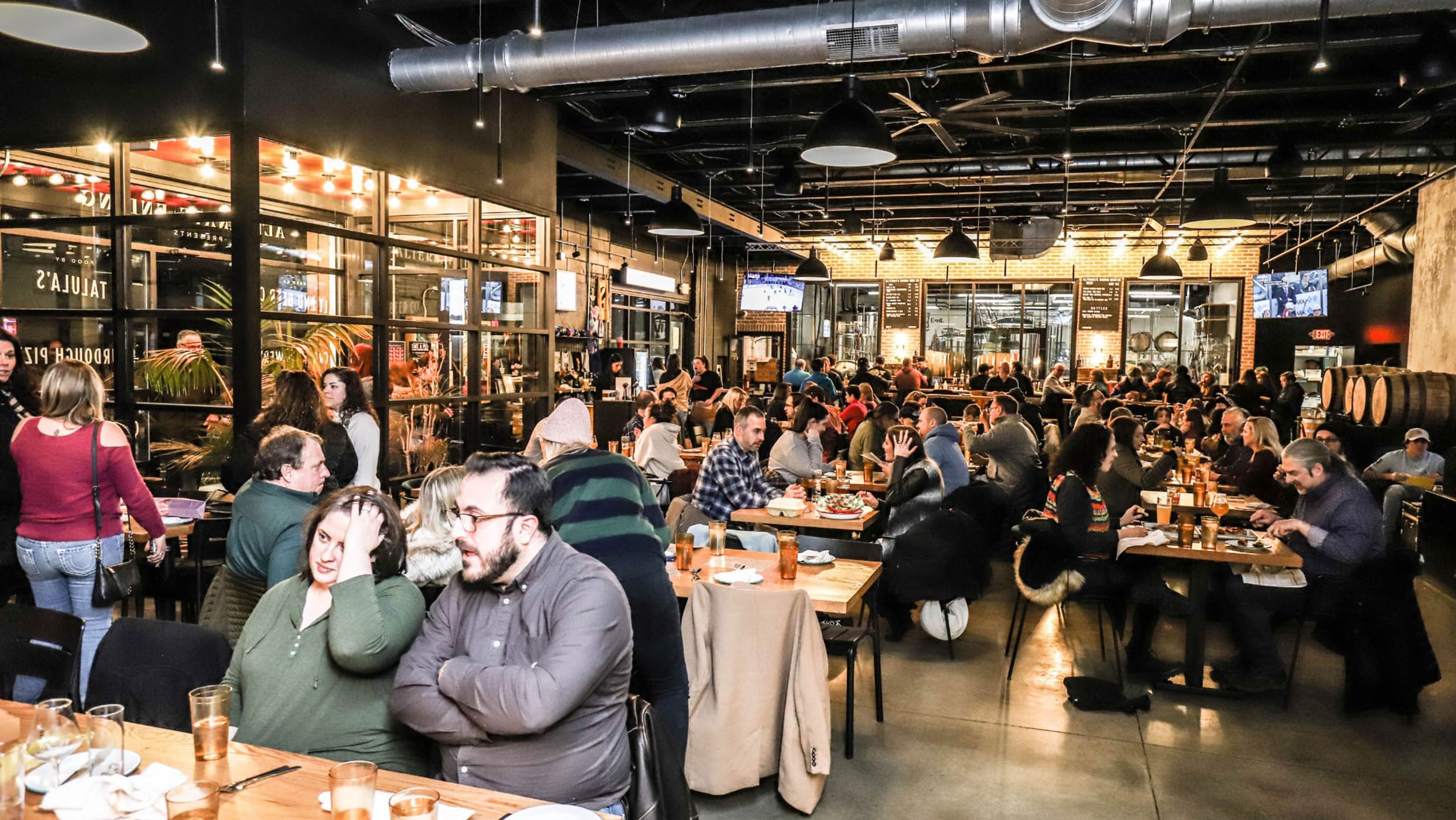Photograph of the inside of a taproom full of tables seated with customers.