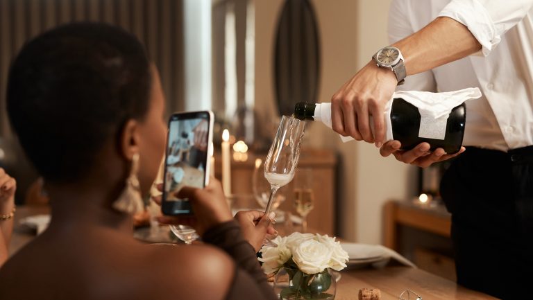 A woman films someone pouring a sparkling wine into her glass on her phone