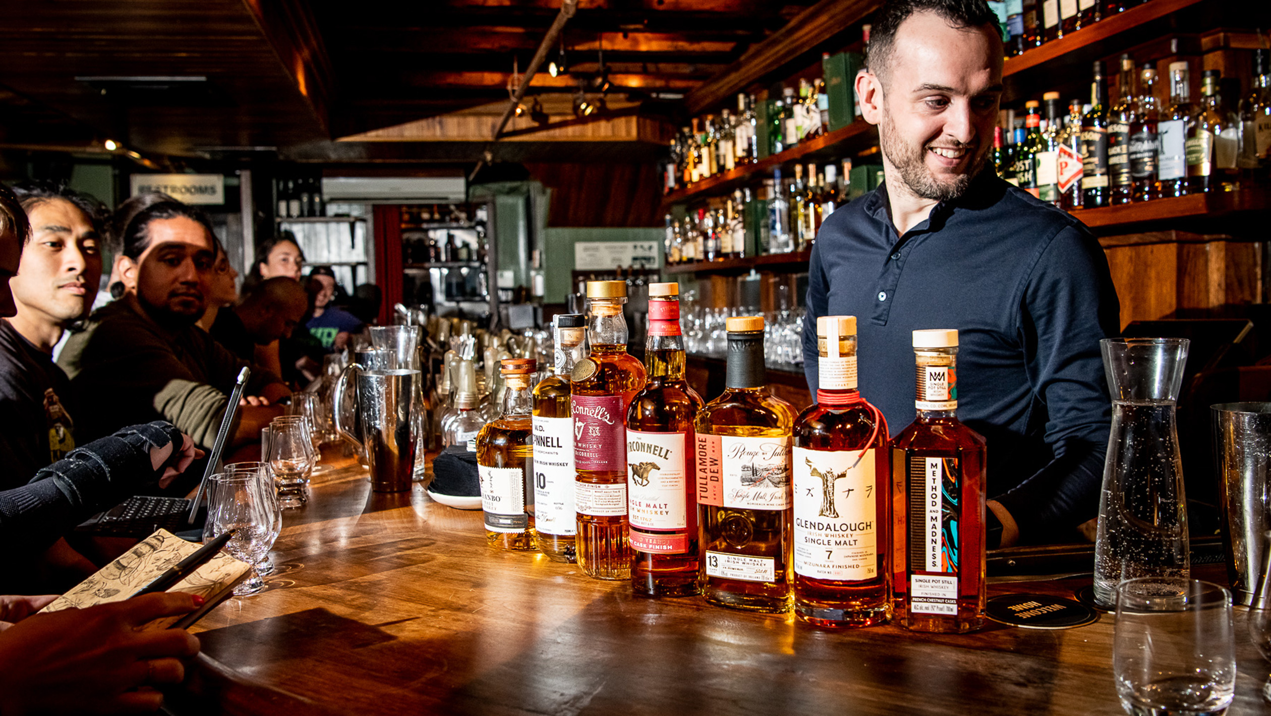 A candid photo of Mark McLaughlin behind the bar with a lineup of Irish whiskey on the bartop in front of him