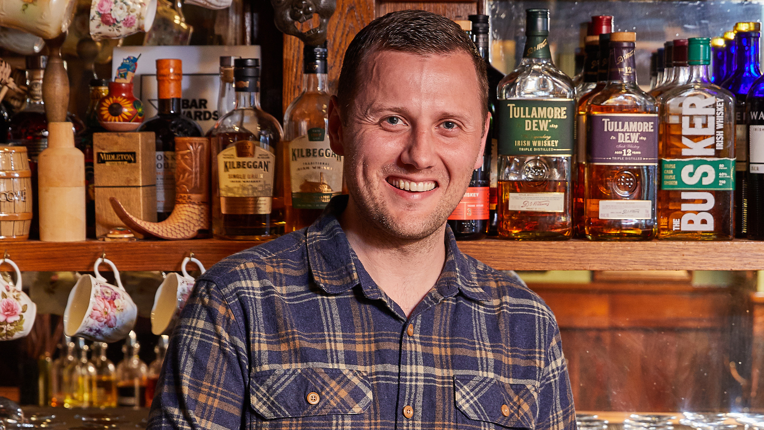 Headshot of Jack McGarry in front of shelves of whisky
