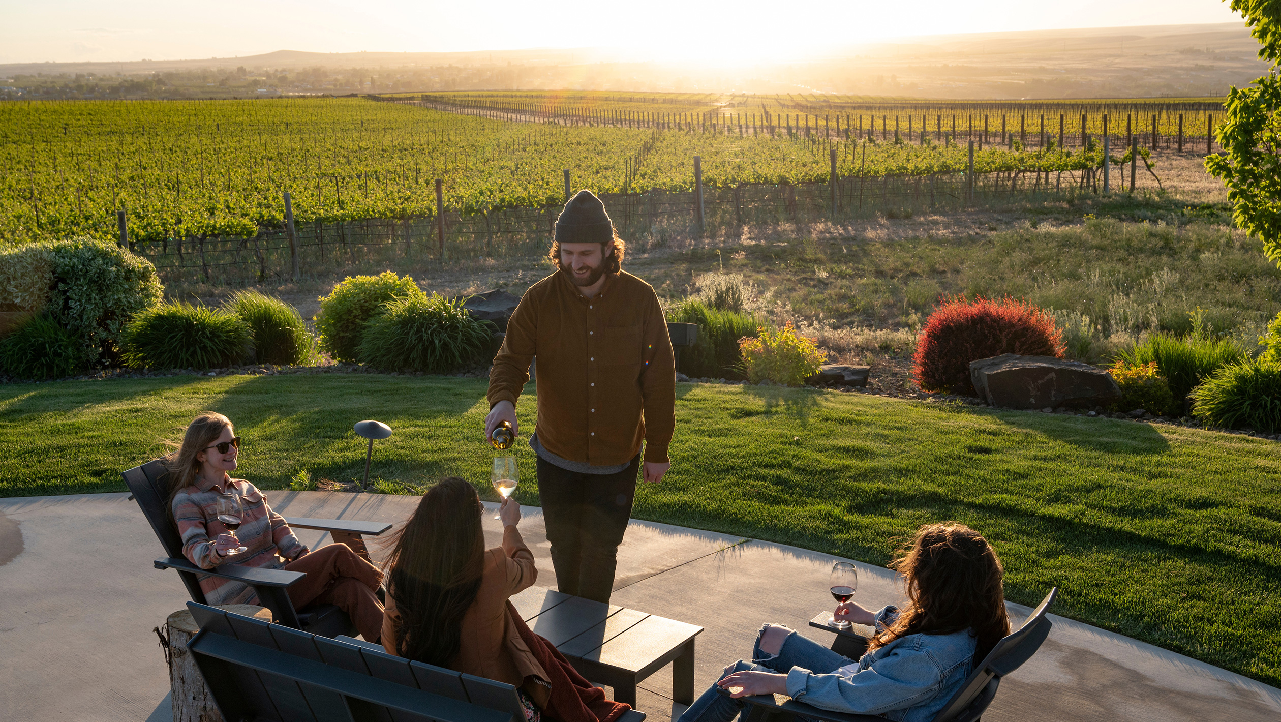 A group of wine drinkers relax in front of a Washington state vineyard before sunset