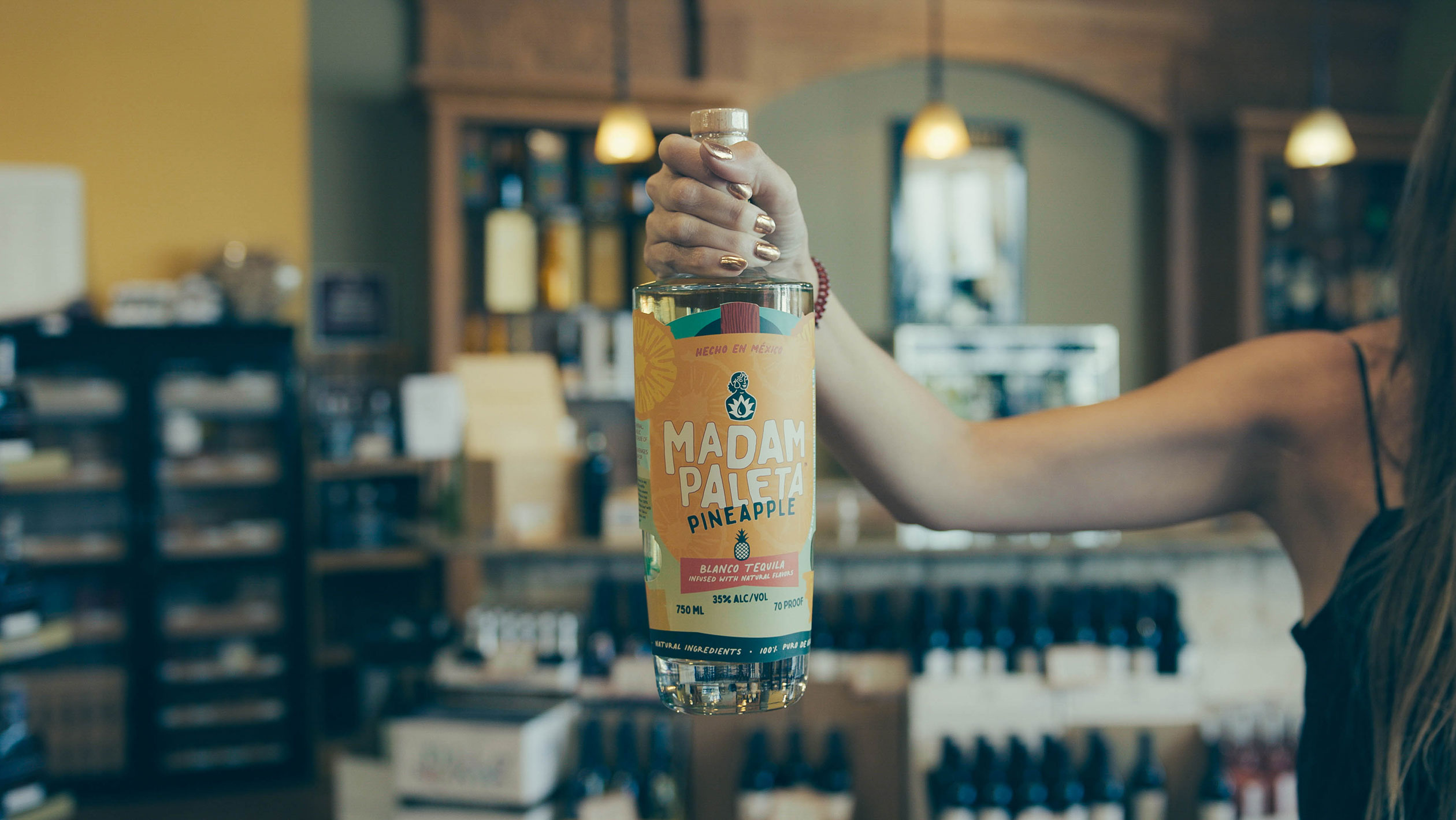 A hand holds up a bottle of Madam Paleta's pineapple-infused tequila