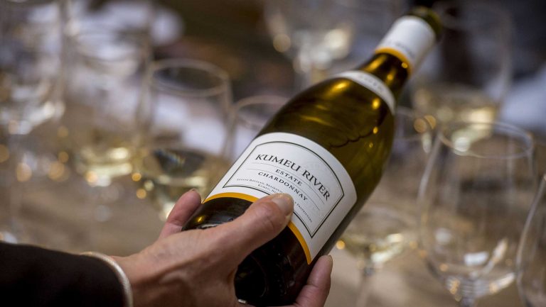 A bottle of New Zealand Chardonnay is poured into multiple wine glasses.