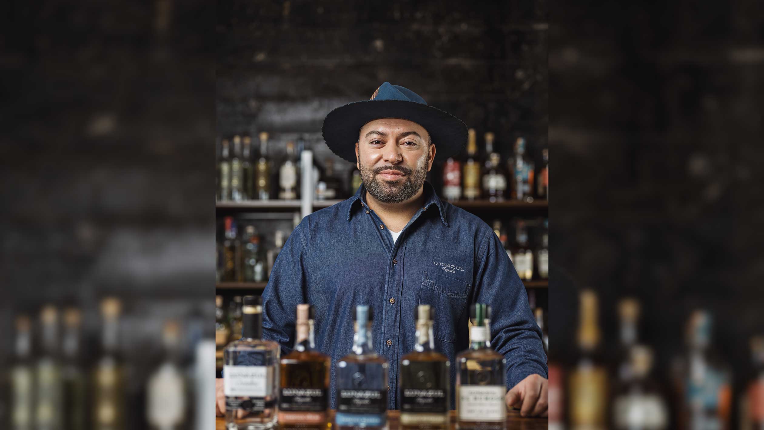 A headshot of Joe Frade as he poses behind a bar with bottles of Lunazul tequila set in front of him.
