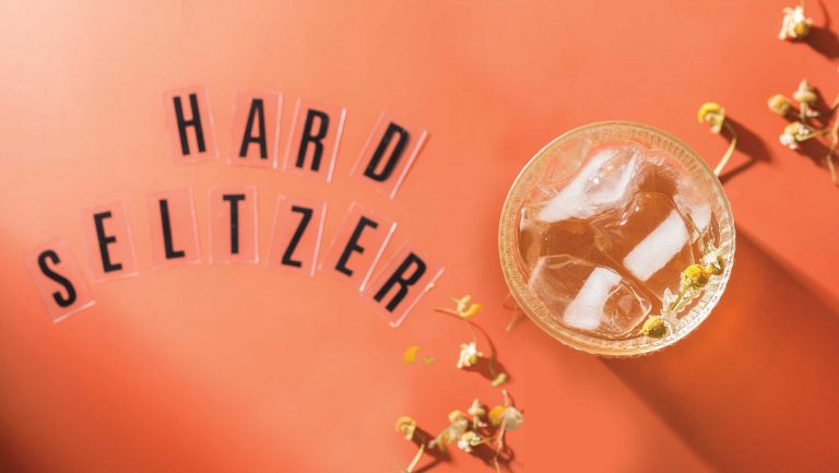 A glass of hard seltzer photographed from above with the words "HARD SELTZER" arranged with marquee lettering