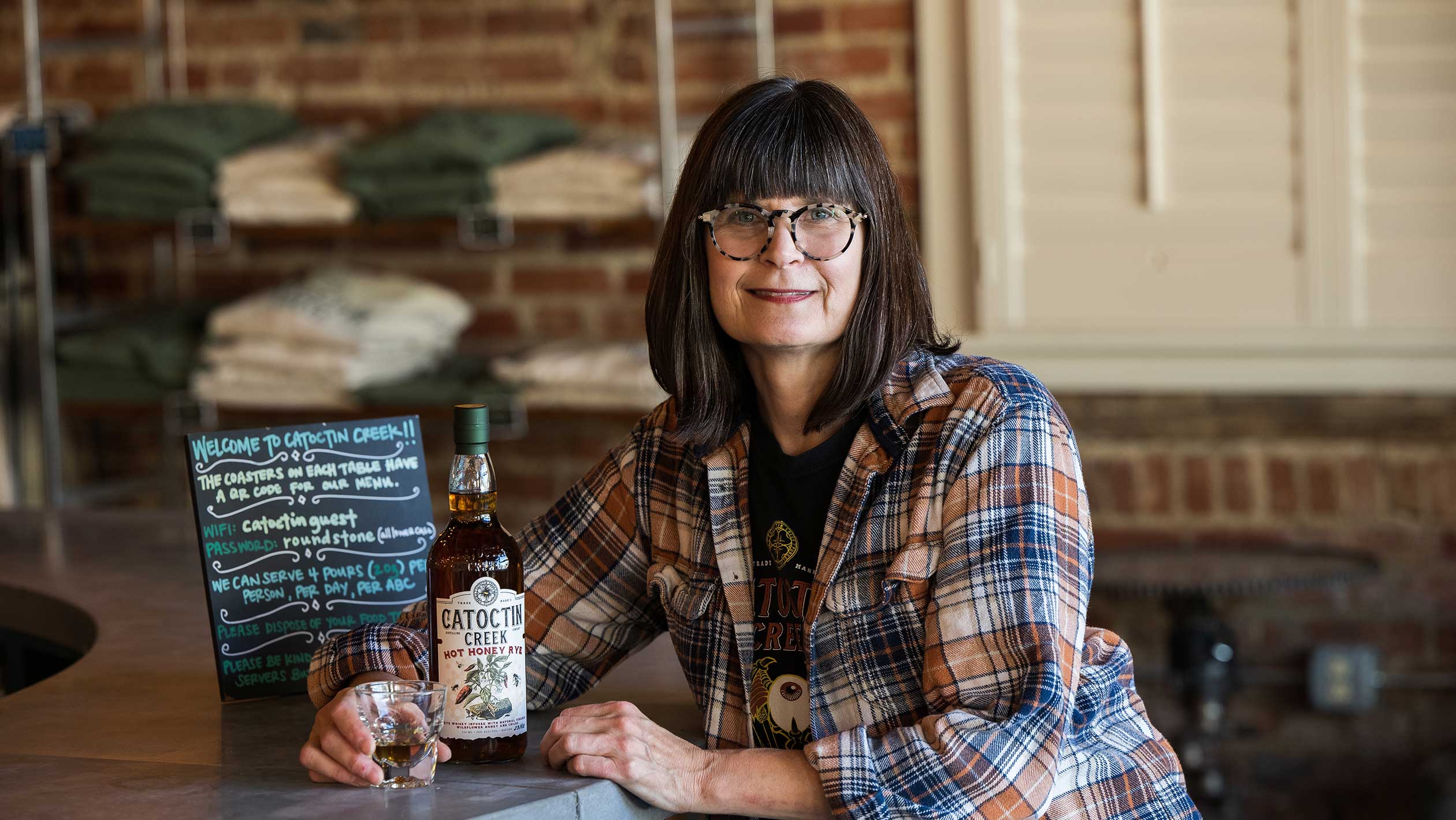 A headshot of Becky Harris as she sits at a bar with a Catoctin Creek Distillery bottle