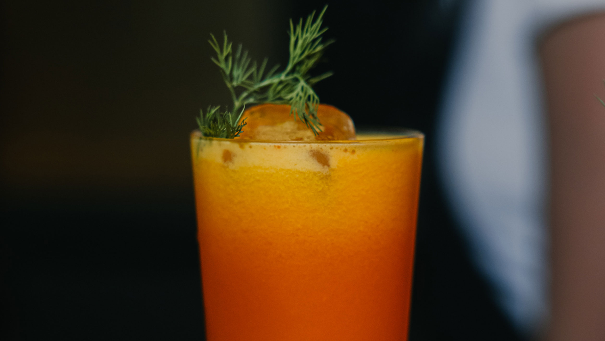 A close up of an orange cocktail garnished with a green herb