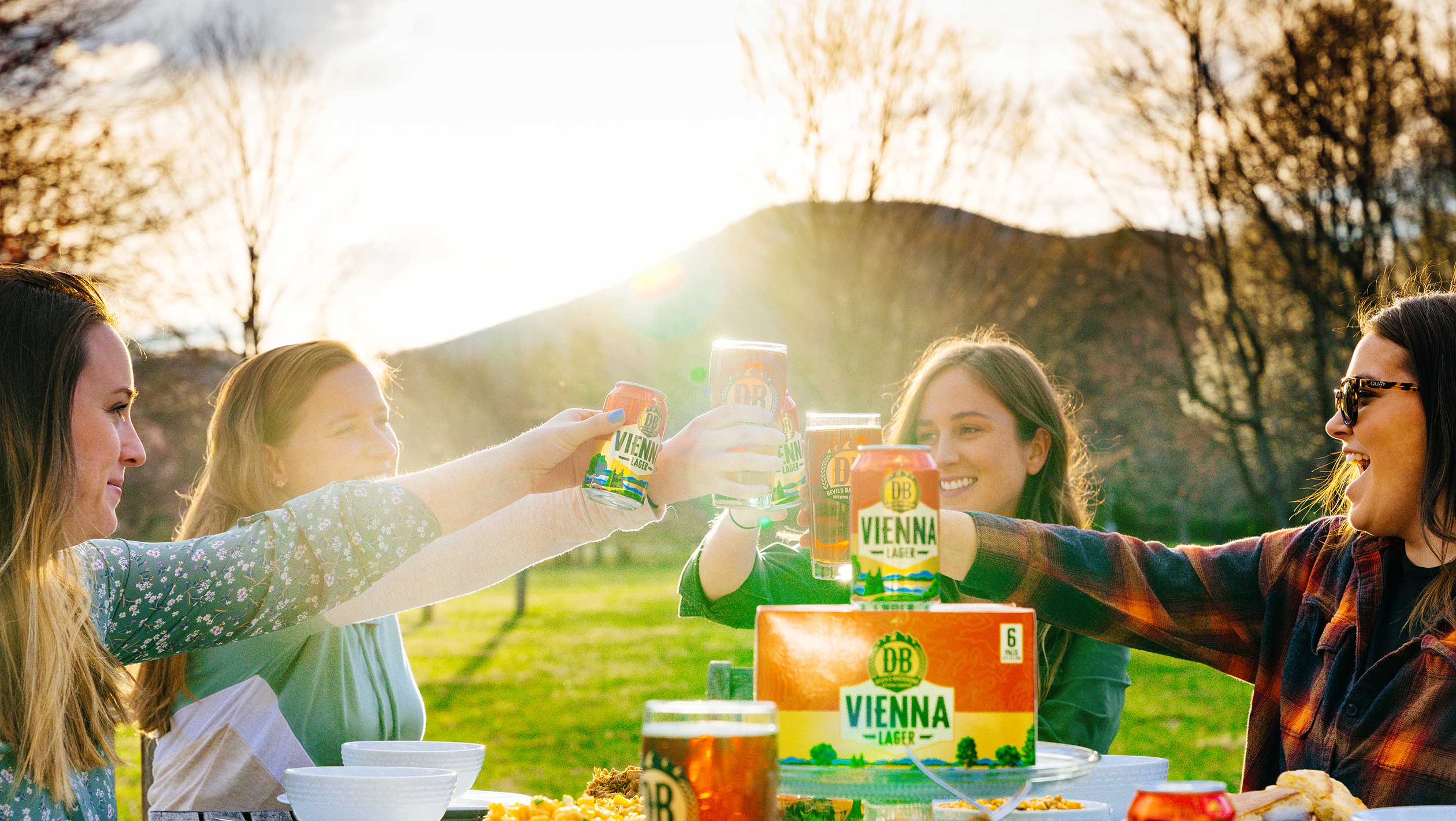 A picturesque photo of a group of women toasting Devils Backbone beers in an outdoor setting