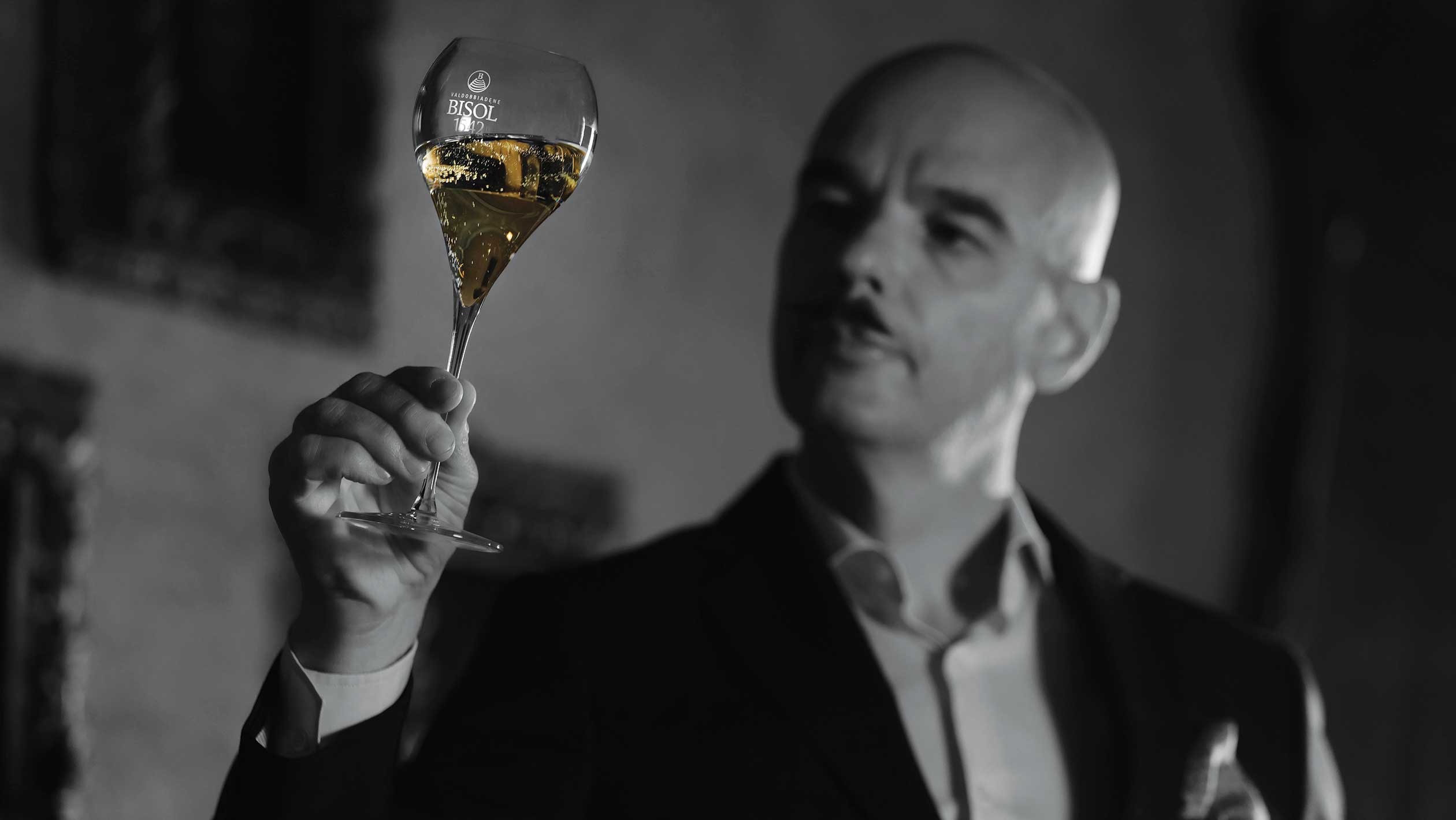 Black and white headshot of Gianluca Bisol as he observes a glass of wine