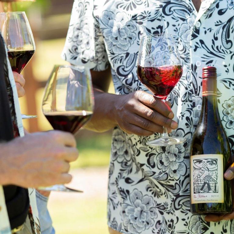 A close up of hands holding glasses and a bottle of ROCO Stalker Pinot Noir