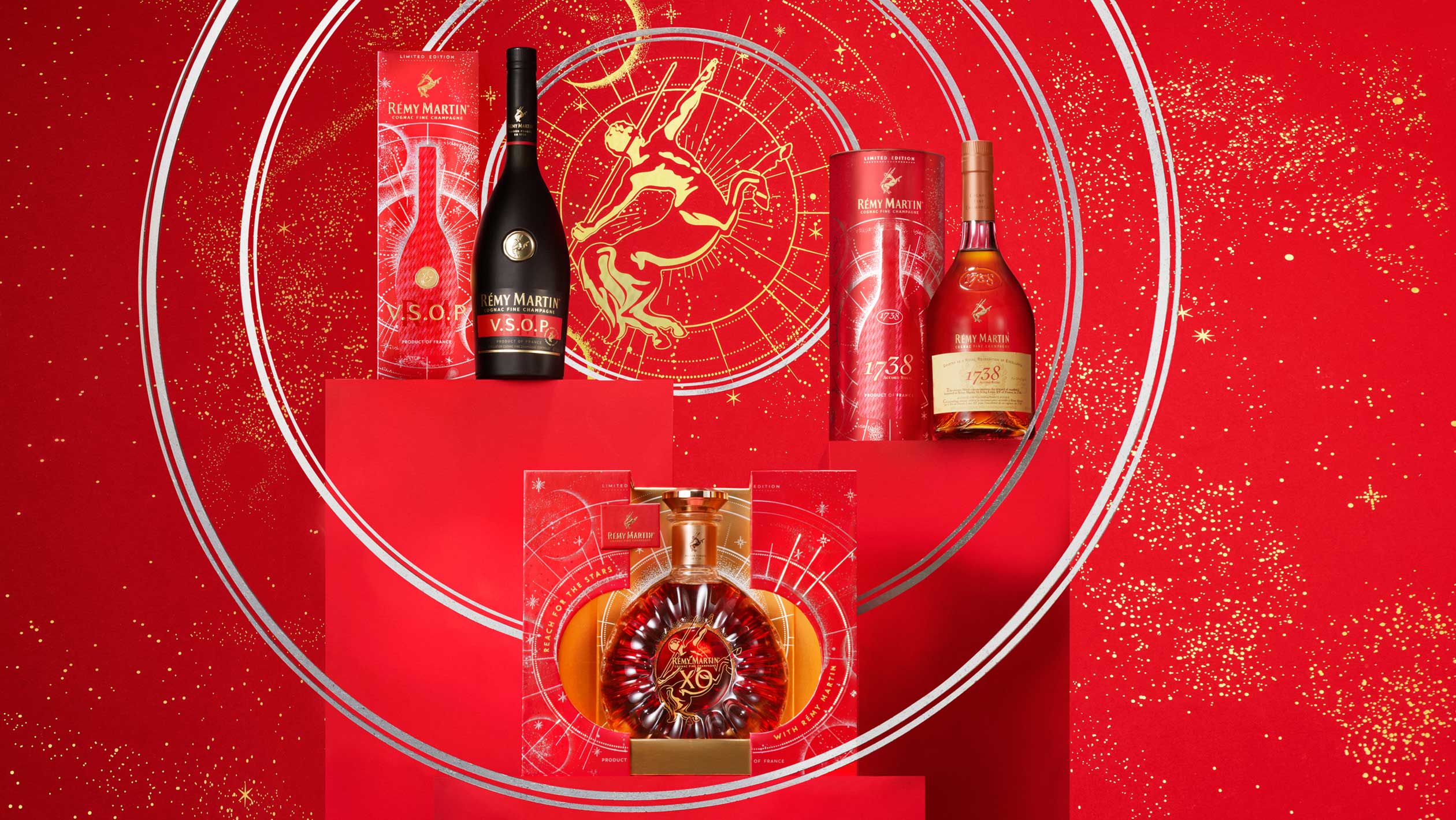 A promotional photograph of Rémy Martin's holiday products, which feature astrological themes on a bright red background