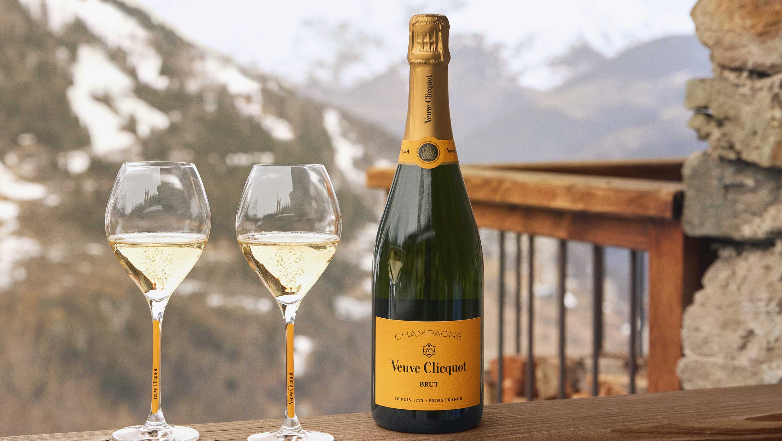 An outdoor photo of a bottle of Veuve Clicquot next to two wine glasses filled with Veuve Clicquot 