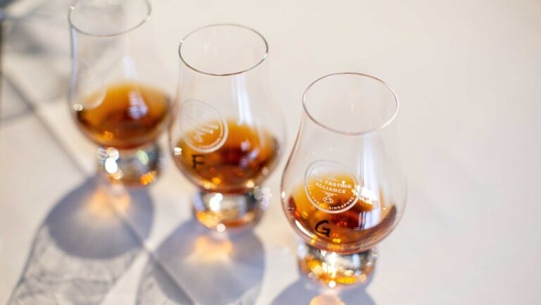Three tasting samples of whiskey sit in Glencairn glasses for judging.