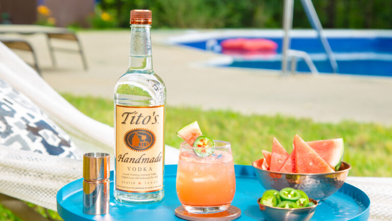 A bottle of Tito's vodka on a tray with a cocktail.