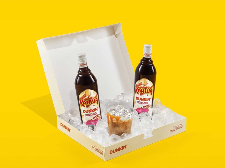 Two bottles of Kahlúa Dunkin’ Caramel Swirl Cream Liqueur in a gift box with a glass of the drink on ice.