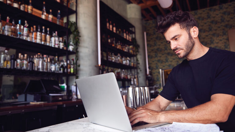 A man at a laptop in a bar or restaurant.