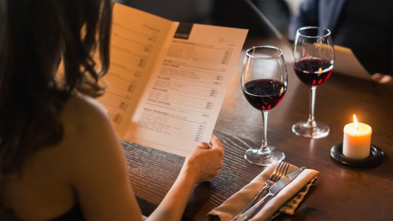 A woman reading the menu with a glass of red wine by candlelight.