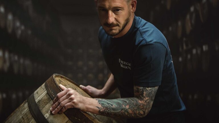 Tattooed man moving a barrel.