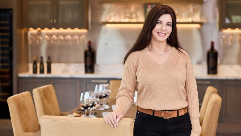 A woman, Ellie Anest, in front of a table set with wines.